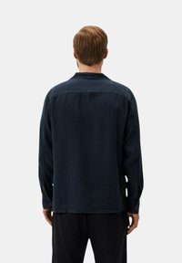 Camisa de manga larga en un azul marino oscuro con un corte relajado, confeccionada en una tela suave. Presenta un cuello tipo solapa y puños abotonados.