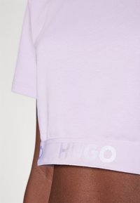 T-shirt court lavande en tissu doux, avec un col rond et une bande de logo blanche à l'ourlet avec un léger éclat.