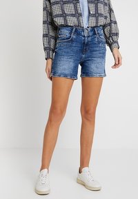 Jeansshorts i ljusblått, med hög midja, två framfickor och uppvikta fållar. Matchas med en mönstrad långärmad skjorta.