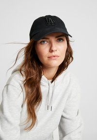 Gorra de béisbol negra con el logo "LA" bordado en la parte frontal, hecha de tejido suave. Presenta una visera curva y una correa ajustable en la parte posterior.