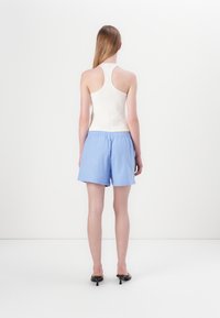 Witte haltertop gecombineerd met lichtblauwe gestreepte shorts. De shorts hebben een elastische tailleband en het materiaal lijkt licht van gewicht te zijn.