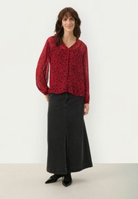 Blusa de manga larga con patrón floral rojo, combinada con una falda de mezclilla negra de tiro alto que tiene una abertura delantera y zapatos negros.