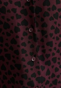 Blusa bordeaux con un motivo a cuori neri, dotata di chiusure a bottoni in plastica coordinata, realizzata in un tessuto leggero e morbido.