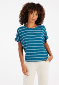 Trumpa rankovėmis, mėlynos spalvos smėlio juostomis ir baltomis linijomis marškiniai, su apvaliu iškirpimu, laisvos apimties, derinami su šviesių spalvų, minkštais vilnoniais keliais.