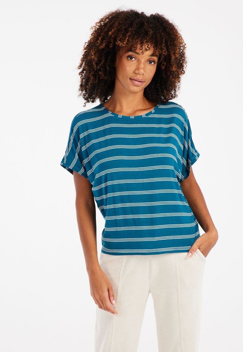 Trumpa rankovėmis, mėlynos spalvos smėlio juostomis ir baltomis linijomis marškiniai, su apvaliu iškirpimu, laisvos apimties, derinami su šviesių spalvų, minkštais vilnoniais keliais.