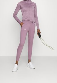 Jasnofioletowa bluzka sportowa z zamkiem błyskawicznym do połowy i długimi rękawami, zestawiona z dopasowanymi legginsami w tym samym kolorze, które mają dwie kieszenie i ściągacze.