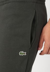 Sweatpants i mørkegrå bomuldsblanding med en sidelomme og et lille grønt broderet krokodillelogo på venstre lår.