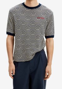 Pletená košile s krátkým rukávem s geometrickým vzorem v krémové a námořnické modré, s kulatým límcem a kontrastními manžetami v námořnické modré. Vyšívané logo.