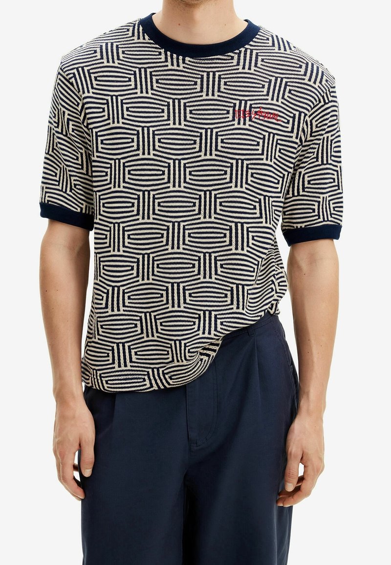 Pletená košile s krátkým rukávem s geometrickým vzorem v krémové a námořnické modré, s kulatým límcem a kontrastními manžetami v námořnické modré. Vyšívané logo.