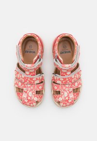 Røde sandaler med blomstermønster, flere spenner, polstret fotseng og borrelås. Har gummisåle for godt grep.