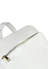 Witte textuurleren rugzak met een gouden rits en handvat aan de bovenkant, dichtbij weergegeven tegen een witte achtergrond.