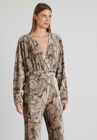 Mono marrón estampado con manga larga, escote en V, cintura ceñida con cinturón y tejido texturizado que presenta un diseño ondulado en tonos claros y oscuros.