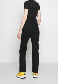 Pantaloni neri a vita alta con un design a gamba dritta, realizzati in denim, dotati di due tasche posteriori e abbinati a scarpe gialle.