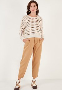 Suéter de punto beige con patrones de puntos abiertos, combinado con pantalones taper fit en color beige. Zapatillas blancas con detalles en marrón completan el look.