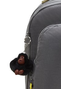 Grauer Rucksack mit strukturierter Oberfläche; ausgestattet mit einem runden schwarzen Gorilla-Schlüsselanhänger mit braunen Gesichtsdetails und zwei kleinen weißen Augen.