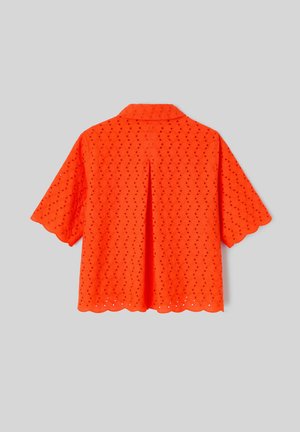 Blouse orange vif à manches courtes en tissu ajouré, bords festonnés, pli au dos et col classique sur fond gris.
