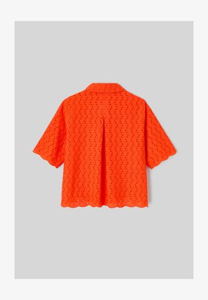 Blouse orange vif à manches courtes en tissu ajouré, bords festonnés, pli au dos et col classique sur fond gris.