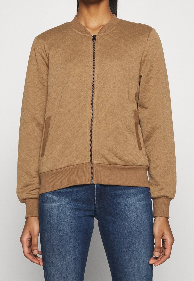 Veste bombardier matelassée marron avec fermeture éclair, poignets et ourlet côtelés, et poches latérales. Elle présente un tissu texturé avec un motif en losanges.