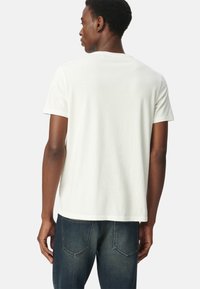 Camiseta blanca de algodón con mangas cortas, cuello redondo clásico y un corte relajado. Combinada con jeans azul oscuro, mostrando un diseño minimalista.