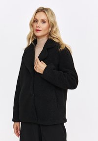 Czarna kurtka z sztucznego futra o luźnym kroju, szerokimi klapami i mi�ękkiej teksturze. Posiada boczne kieszenie i minimalistyczny design.