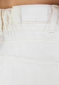 Shorts de mezclilla blanca con una cintura ajustada, que presentan una etiqueta de cuero blanca grabada con "Bershka" y costuras en contraste. Tela texturizada.
