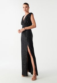 Sort pailette aftenkjole med dyb V-hals, ærmelængde til cap-sleeves og høj slids ved låret. Glat tekstur med en tætsiddende silhuet og samlet talje.