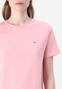 T-shirt in cotone rosa chiaro con scollatura rotonda e maniche corte. Presenta un piccolo logo ricamato sul petto per un tocco di originalità.