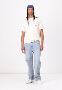 Cream short-sleeve t-shirt, blue beanie, light blue jeans, and white sneakers. Casual fit with relaxed design and soft texture.
