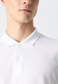 Polo blanco hecho de una tela texturizada, con un cuello clásico, dos botones y un sutil logo "BOSS" en el pecho.