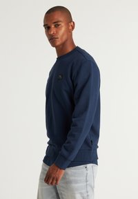 Felpa blu navy con scollo tondo, maniche lunghe e un piccolo logo nero sul petto, realizzata in tessuto testurizzato.
