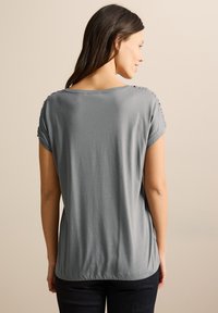 Top gris de manga corta con un ajuste relajado, que presenta acentos texturizados en las costuras de los hombros y un escote redondeado. Textura de tela suave.