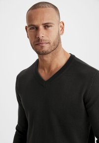 Schwarzer V-Ausschnittpullover, Strukturstrick, lange Ärmel, enganliegendes Design. Glattes Material, minimale Nähte und eine klassische Silhouette.