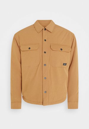 Šviesiai ruda mygtukinė striukė su tiesiu apykakle, dviem krūtinės kišenėmis ir juodais snapeliais. Sklandi tekstūra ir apvalus kraštas apačioje.