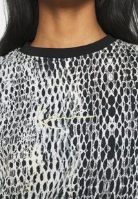 Koszulka z krótkim rękawem z wzorem w czarno-białe węże, o strukturalnej powierzchni i zielonym haftowanym logo z przodu.