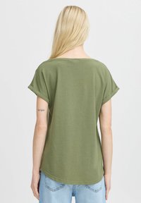 Camiseta de manga corta verde oliva con un ajuste relajado y puños enrollados, con un dobladillo ligeramente curvado y una textura de algodón suave.