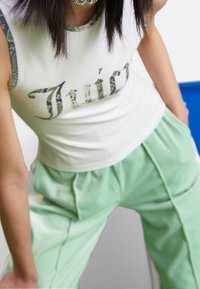 Bílý bezrukávový top s límcem s potiskem zeleného hada, se znakem "Juicy". V kombinaci s volnými kalhotami světle mátové barvy. Minimální textura.