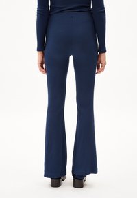 Pantalones acampanados de canalé azul marino con una textura suave, que presentan una costura trasera y se combinan con botas negras de suela gruesa.