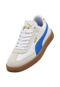 Zapatilla blanca con detalles en ante azul, logo dorado y cordones blancos. Presenta una suela de goma texturizada y parte superior de cuero liso.