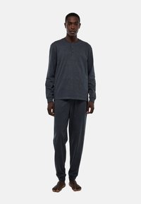 Chemise à manches longues gris foncé avec un col henley boutonné, associée à un pantalon gris assorti. Tissu doux, coupe décontractée et design minimal.