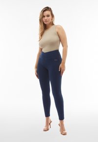 Leggings azul marino con una cintura alta, fabricados con material elástico. Textura suave con una silueta ajustada y detalle de costura lateral.