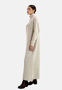 Abito a collo alto in maglia beige con texture a coste e maniche lunghe, abbinato a stivaletti alla caviglia marrone scuro.