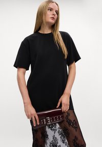 Czarna, oversize t-shirt z krótkim rękawem, w połączeniu z ciemnoczerwoną kopertówką z metalowymi detalami w kolorze srebrnym oraz sercowymi ćwiekami, warstwowo na przezroczystej koronkowej bluzce.