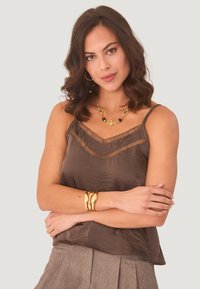 Camisón de satén marrón con bordes de encaje y tirantes finos. Combinado con joyería dorada y una falda gris texturizada y plisada.