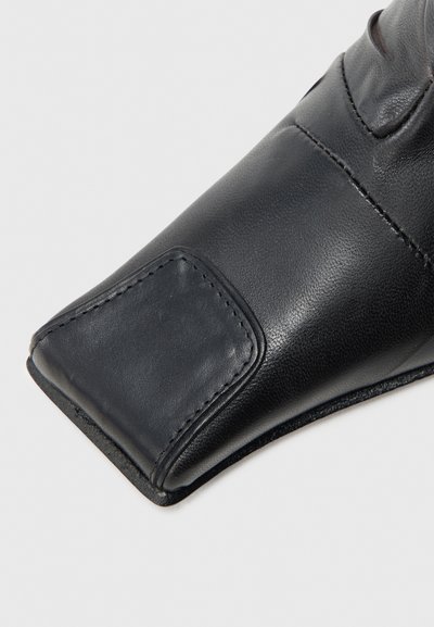 Melna ādas cimdi ar gludu tekstūru, ar šuvju detaļām un pastiprinātu lauku plaukstas pusē, lai nodrošinātu lielāku izturību.