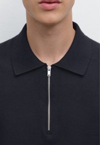 Marinblå zip-up polo skjorta tillverkad av textiliserat material, med en platt krage och en silverfärgad dragkedja med en subtilt kontrasterande söm.