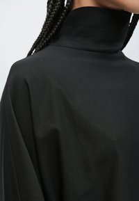 Černý rolák z hladké, měkké látky s volným střihem, jemným leskem a minimálními švy.