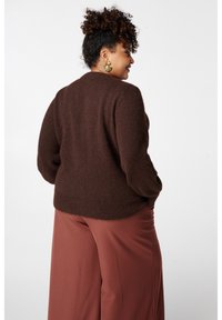 Pull en tricot marron à coupe décontractée, avec ourlet côtelé et manches longues, associé à un pantalon ample de couleur rouille.