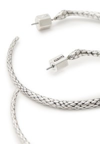 Pendientes trenzados de plata con un diseño texturizado. Presentan acentos cilíndricos de plata en cada extremo. Acabado metálico suave.