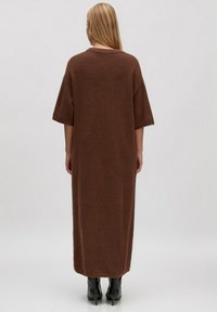 Braunes, übergroßes Strickkleid mit kurzen Ärmeln, strukturiertem Stoff und gerader Silhouette, das bis zur Mitte der Wade reicht. Getragen mit schwarzen, hohen Stiefeln.