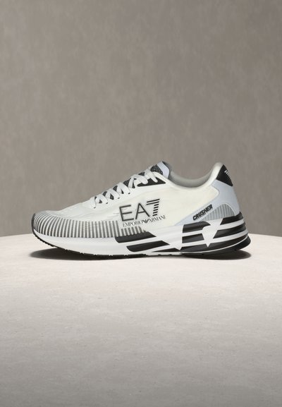 Бяла и черна маратонка Emporio Armani EA7 с логотип, с шарена подметка и връзки, изложена на неутрална повърхност и фон.